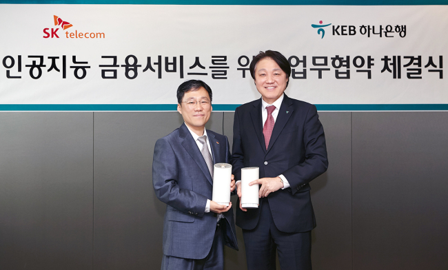 Lee Sang-ho (left), head of AI business at SK Telecom, and Han Jun-sung, vice president of future finance at KEB Hana Bank, hold up a partnership certificate at the bank’s headquarters in central Seoul on Wednesday. (SK Telecom)