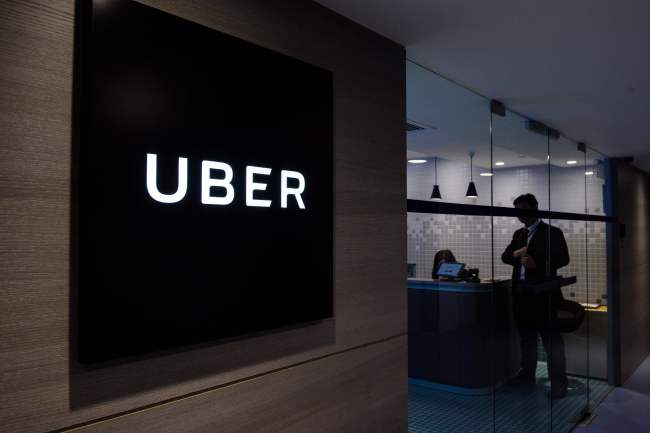 This file photo taken on March 10, 2017 shows Uber signage and an employee standing in the entrance of the ride-hailing giant's office in Hong Kong. (AFP-Yonhap)