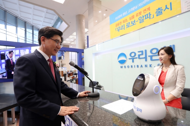 Woori Bank CEO Lee Kwang-goo poses at a counter with a robot run on AI-based financial service Woori Robo-Alpha in a head branch located in Jung-gu, Seoul Wednesday. (Woori Bank)