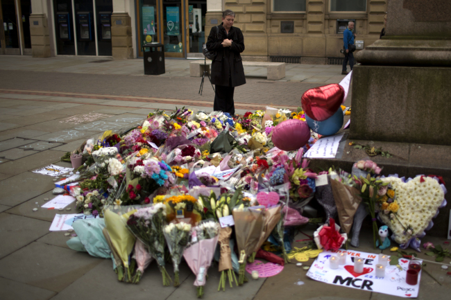A woman stands next to flowers offered for the victims of a suicide attack at a concert by Ariana Grande that killed more than 20 people Monday night in central Manchester, Britain, Wednesday. (AP-Yonhap)