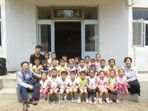 This undated photo, taken from the website of the London-based Love North Korean Children on June 13, 2017, shows the charity group`s leader George Rhee (far L, front) posing for a photo with children during a monitoring visit to the North. (Yonhap)