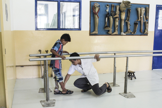 An amputated child receives assistance from an ortho-prosthetist working for the ICRC with a newly fitted prosthetic leg in southern Myanmar. (The International Committee of the Red Cross)