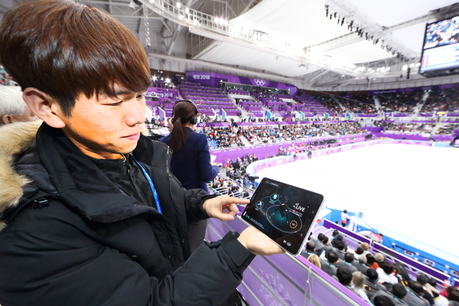 A spectator watches a short track speedskating competition on a device using time slice, a 5G-dependent video streaming technology enabling viewers to control the time, target and angle of the video, with the competition captured at 180 degrees by some 100 cameras set up at Gangneung Ice Arena. Yonhap
