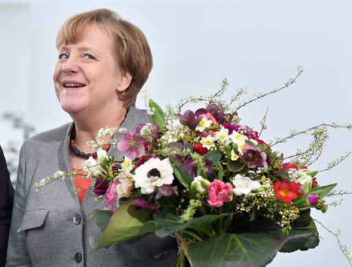 This file photo taken on February 9, 2018 shows German Chancellor Angela Merkel holding a flower bouquet given to her by the President of the German Horticultural Association in the chancellery in Berlin. Long dubbed the 