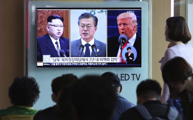People watch a TV screen showing file footage of US President Donald Trump, right, South Korean President Moon Jae-in and North Korean leader Kim Jong Un, left, during a news program at the Seoul Railway Station in Seoul, South Korea, April 18, 2018 (AP)