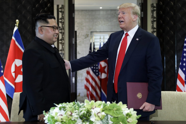 US President Donald Trump reaches for North Korea leader Kim Jong Un after they signed documents at the Capella resort on Sentosa Island on Tuesday. (AP-Yonhap)