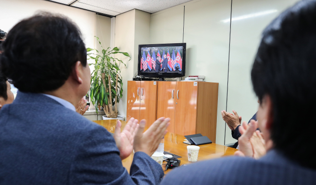 Officials of a corporate meeting on the Kaesong Industrial Complex, under the Korea Federation of SMEs in Seoul, clap as they watch US President Donald Trump and North Korea`s leader Kim Jong-un shake hands at their summit in Singapore, Tuesday. (Yonhap)