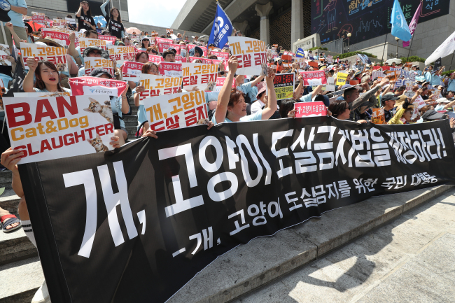 Protesters hold signs asking for the ban of cat and dog slaughter in front of Sejong Center in Jongno-gu on Sunday. (Yonhap)