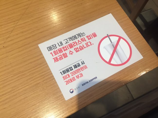 A sign that says in-store customers cannot be given plastic cups for their beverages and that business owners will be subject to a fine of up to 2 million won ($1,769) if they violate the rule is placed on a table at an Ediya Coffee outlet in Seoul. (Claire Lee / The Korea Herald).