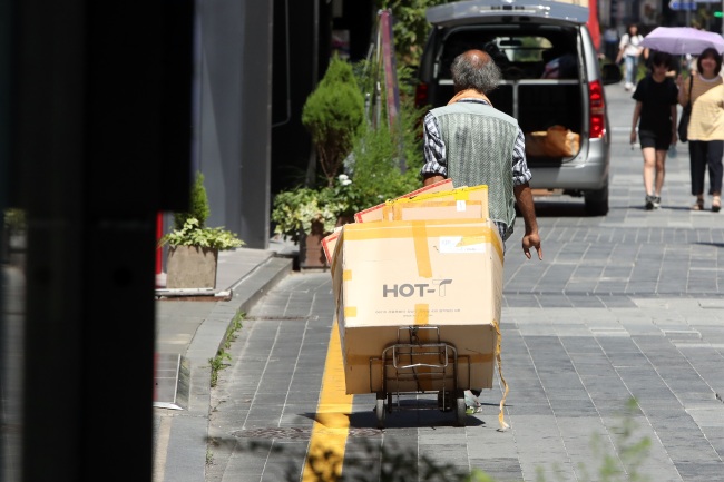 An elderly Korean man carries a cart through the streets, collecting used boxes and cardboard for a living. (Yonhap)