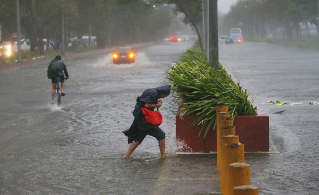 Commuters brave the rain and strong winds brought about by Typhoon Mangkhut which barreled into northeastern Philippines before dawn Saturday, Sept. 15, 2018 in Manila, Philippines. (Yonhap)