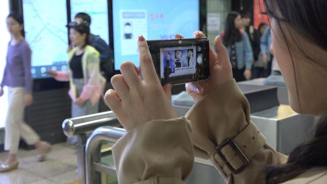 An onlooker at Hongdae Station takes a photo of an ad celebrating BTS member Jimin’s birthday. (Park Ju-young/The Korea Herald)