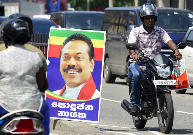 Sri Lankan motorcyclists ride past a poster of Mahinda Rajapakse‘s after he was sworn in as prime minister in Colombo on October 27, 2018. - Sri Lanka President Maithripala Sirisena on October 27 suspended parliament, deepening political turmoil after he sacked the country’s prime minister. (LAKRUWAN WANNIARACHCHI / AFP)