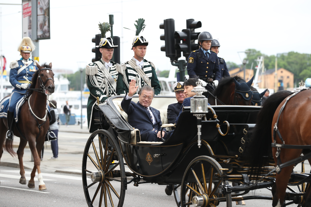 South Korean President Moon Jae-in (L) waves while riding through Stockholm streets in a carriage seated together with King Carl XVI Gustaf for a welcoming ceremony at the Royal Palace on Friday. (Yonhap)