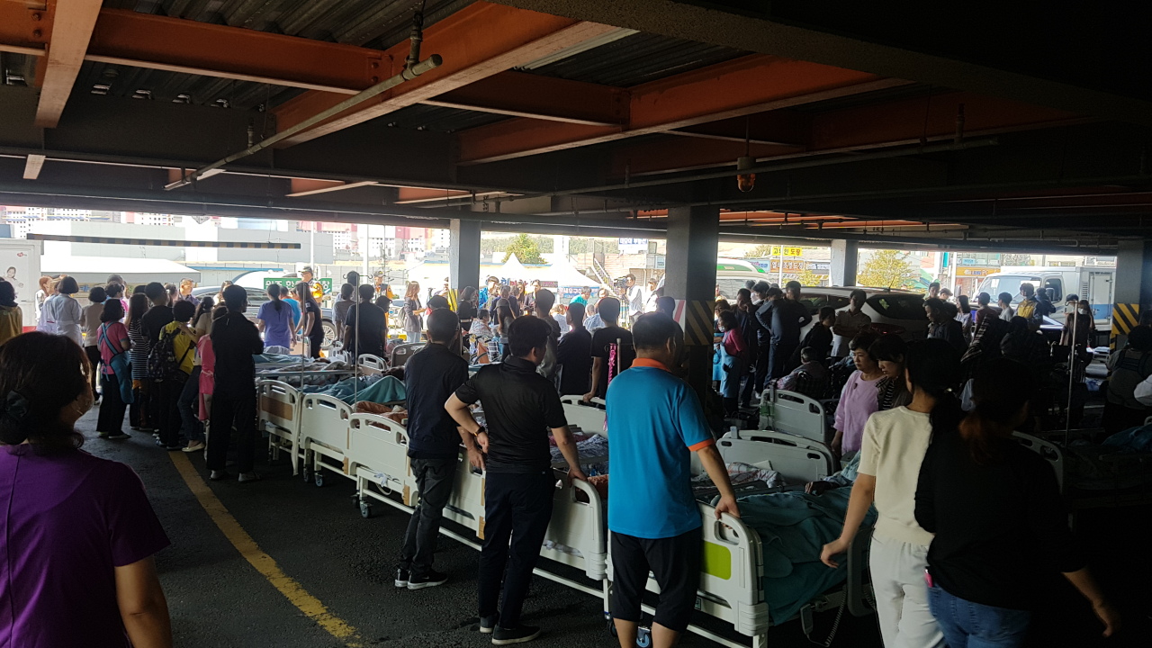 Patients of Gimpo Rehabilitation Clinic in Gyeonggi Province and their family members wait at the building’s parking lot to be transferred to hospital Tuesday. (Choi Ji-won/The Korea Herald)