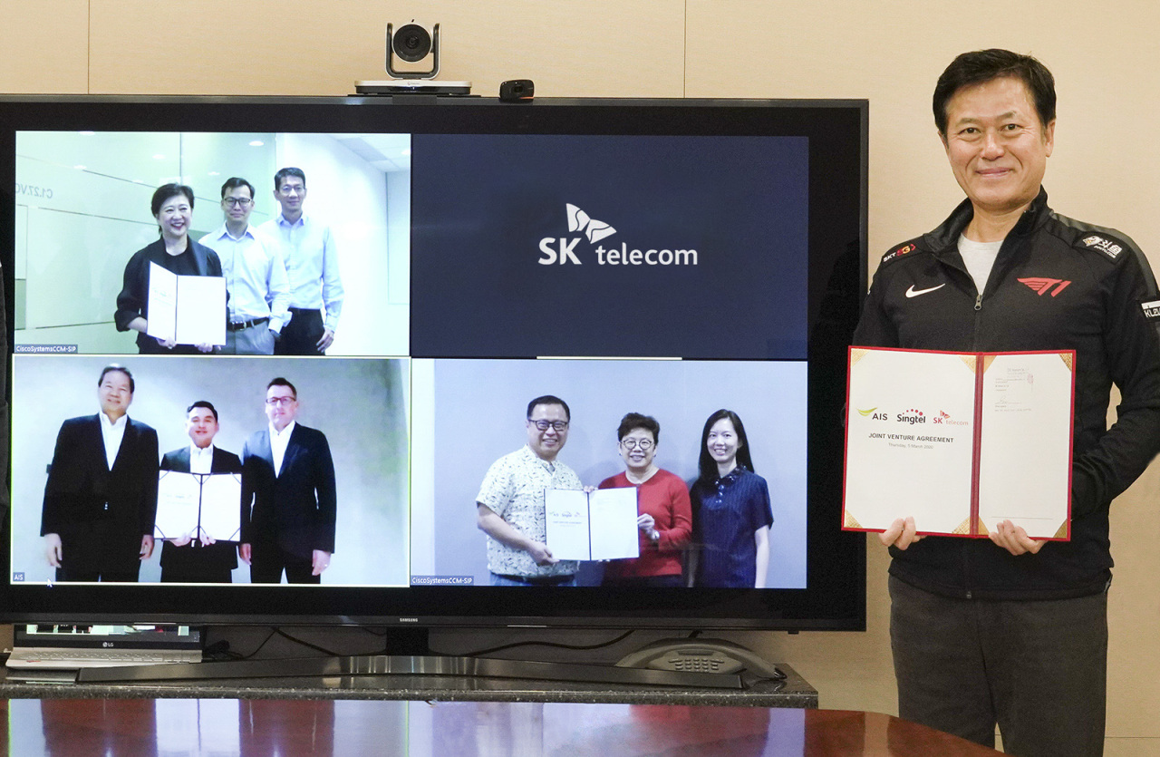 SKT CEO Park Jung-ho holds up the joint venture establishment contract, dressed in the uniform of SKT’s League of Legends esports team T1. Park is joined in the picture by Singtel CEO Chua Sock Koong (left, top) and AIS CEO Somchai Lertsutiwong (left, bottom) via a remote conference. (SKT)