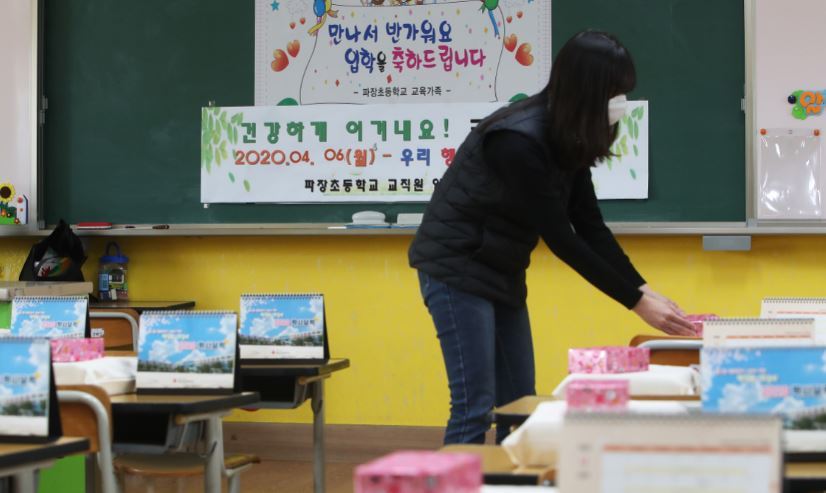 A teacher at an elementary school in Suwon, Gyeonggi Province, lays new textbooks on desks for students on March 17, three weeks before offline classes were to start. But classes are postponed indefinitely amid the ongoing spread of COVID-19. Instead, online classes are to start later this month. (Yonhap)