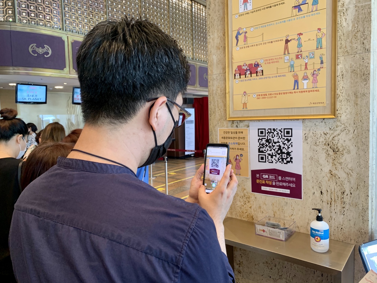 A theatergoer uses a QR code app to fill out a health check form on Friday before entering the concert hall to see “Mozart!” at the Sejong Center for the Performing Arts in Gwanghwamun, central Seoul. (Im Eun-byel/The Korea Herald)