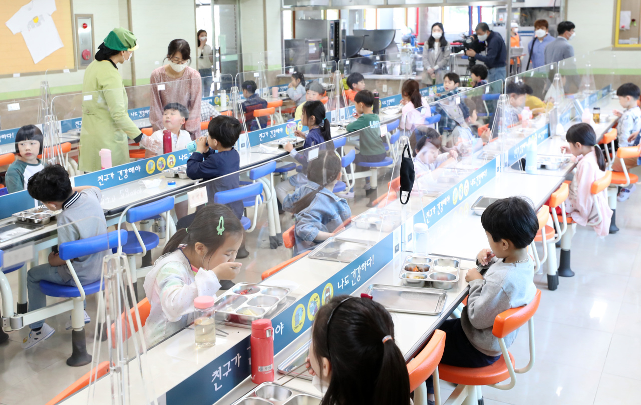Elementary school students eat lunch while seated in a zigzag configuration with partitions at the tables. (Yonhap)