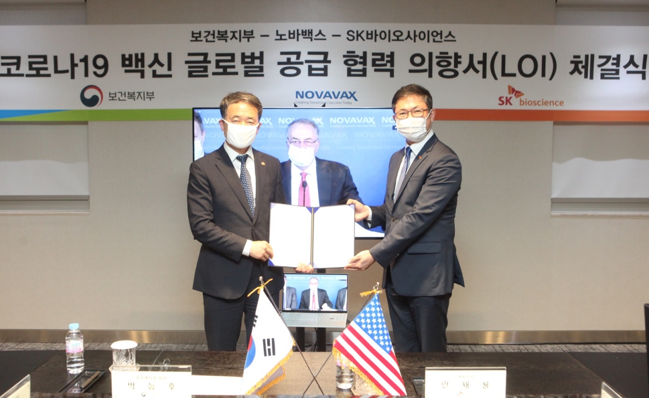 SK Bioscience and Novavax sign a letter of intent at SK Bioscience’s research laboratory in Pangyo, Gyeonggi Province, Thursday. Health Minister Park Neung-hoo (left) shake hands with SK Bioscience CEO Ahn Jae-yong, with Novavax CEO Stanley Erck present via online conference call. (SK Bioscience)