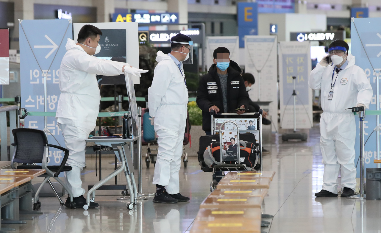 Officials wearing protective suits guide an incoming traveler at the Incheon International Airport on Monday. (Yonhap)