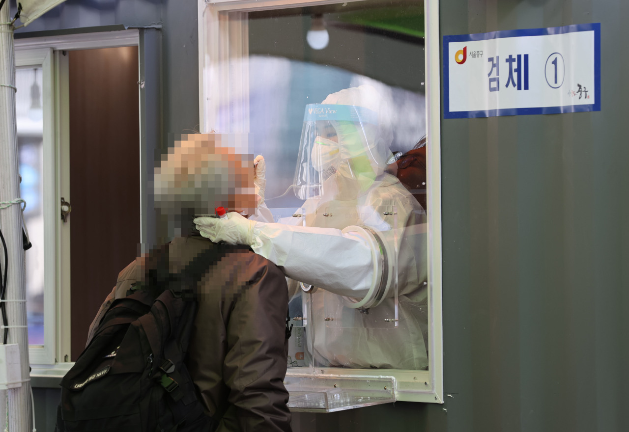 A medical worker in protective suit takes nasal sample as a COVID-19 check Thursday at a diagnostics center made near the Seoul Station.