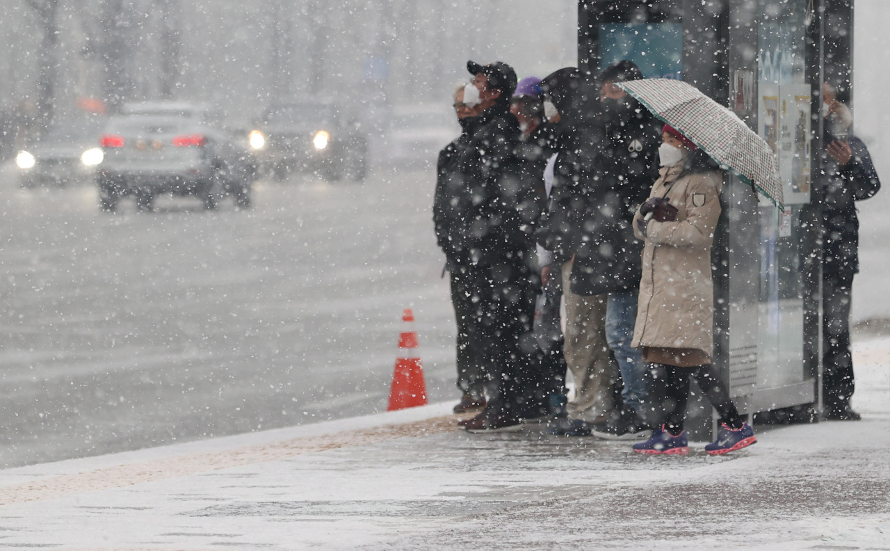 People wait in the snow for buses near Gwanghwamun Square in central Seoul on Tuesday. (Yonhap)
