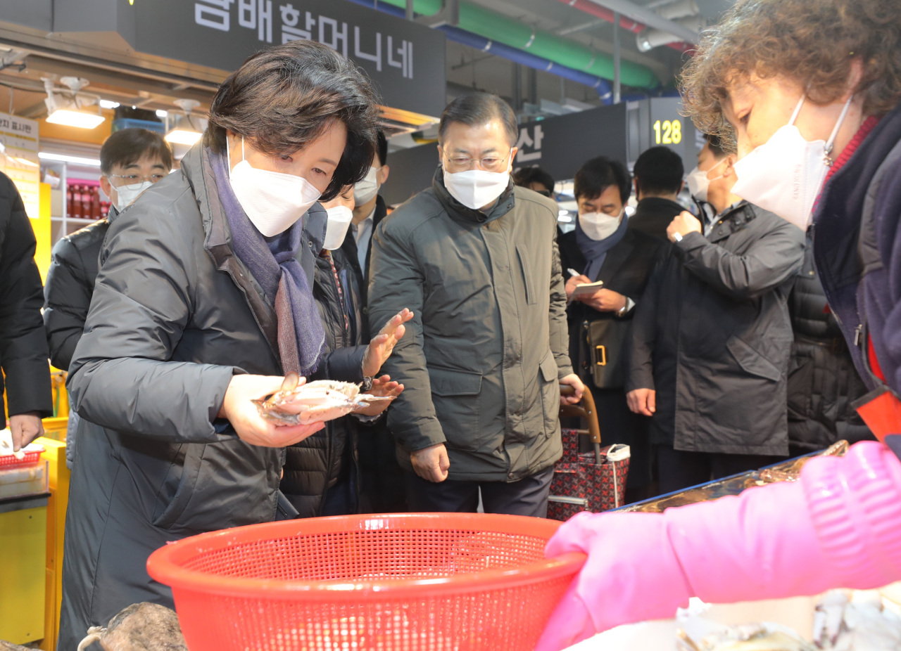 President Moon Jae-in (C) and first lady Kim Jung-sook (L) take a look at fishery products at the Soraepo-gu Fish Market in Incheon, 40 kilometers west of Seoul, on Wednesday. Moon and Kim visited the market to hear out the hardships of small merchants going through tough times due to the new coronavirus and encourage them ahead of the Lunar New Year holiday. (Yonhap)