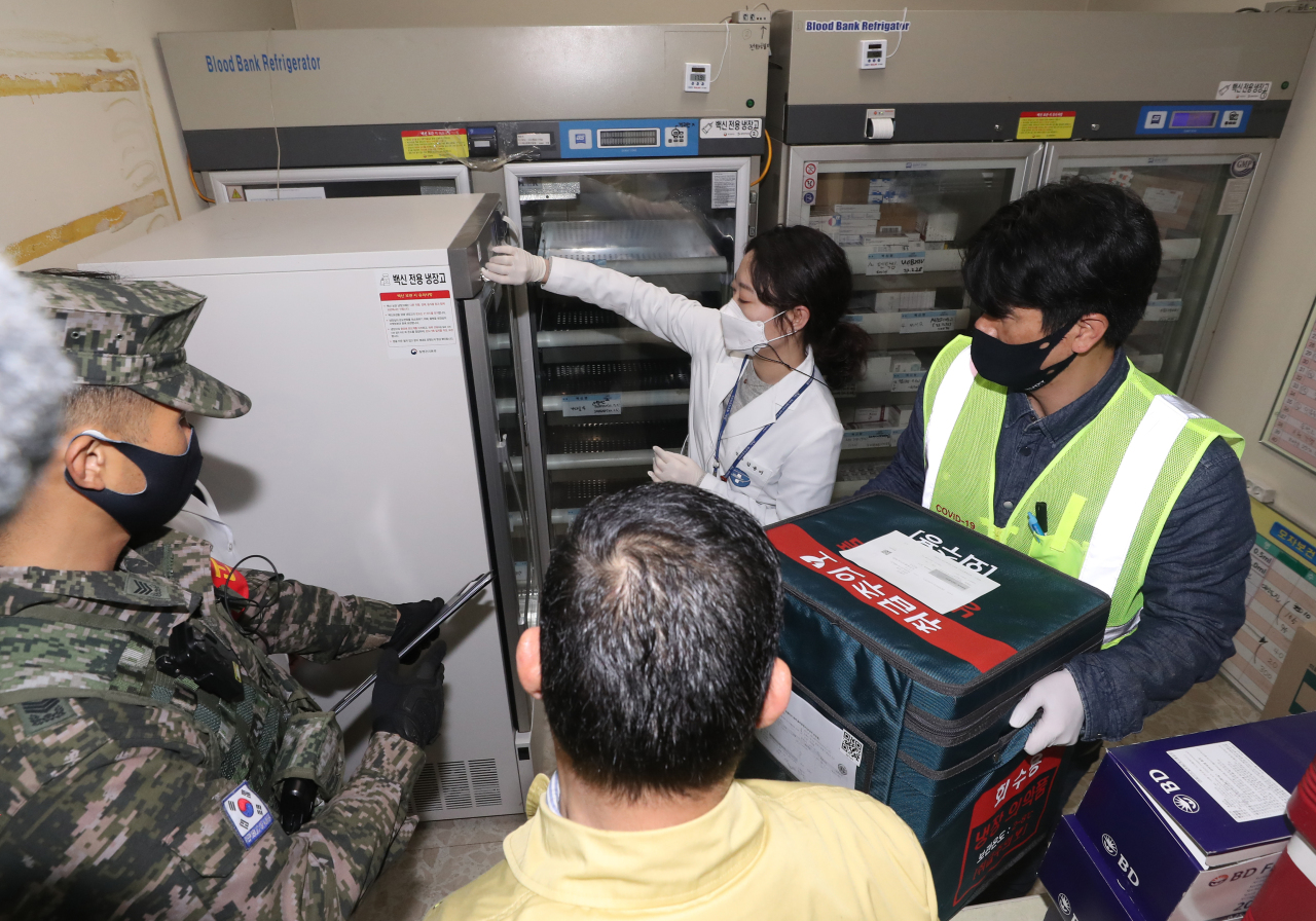 An official moves a box containing AstraZeneca's vaccine to a medical worker under the escort of the military and police after arriving at a public health center on the country's southern Jeju Island in the wee hours of Thursday, one day ahead of the start of the COVID-19 vaccination of the whole nation. (Yonhap)