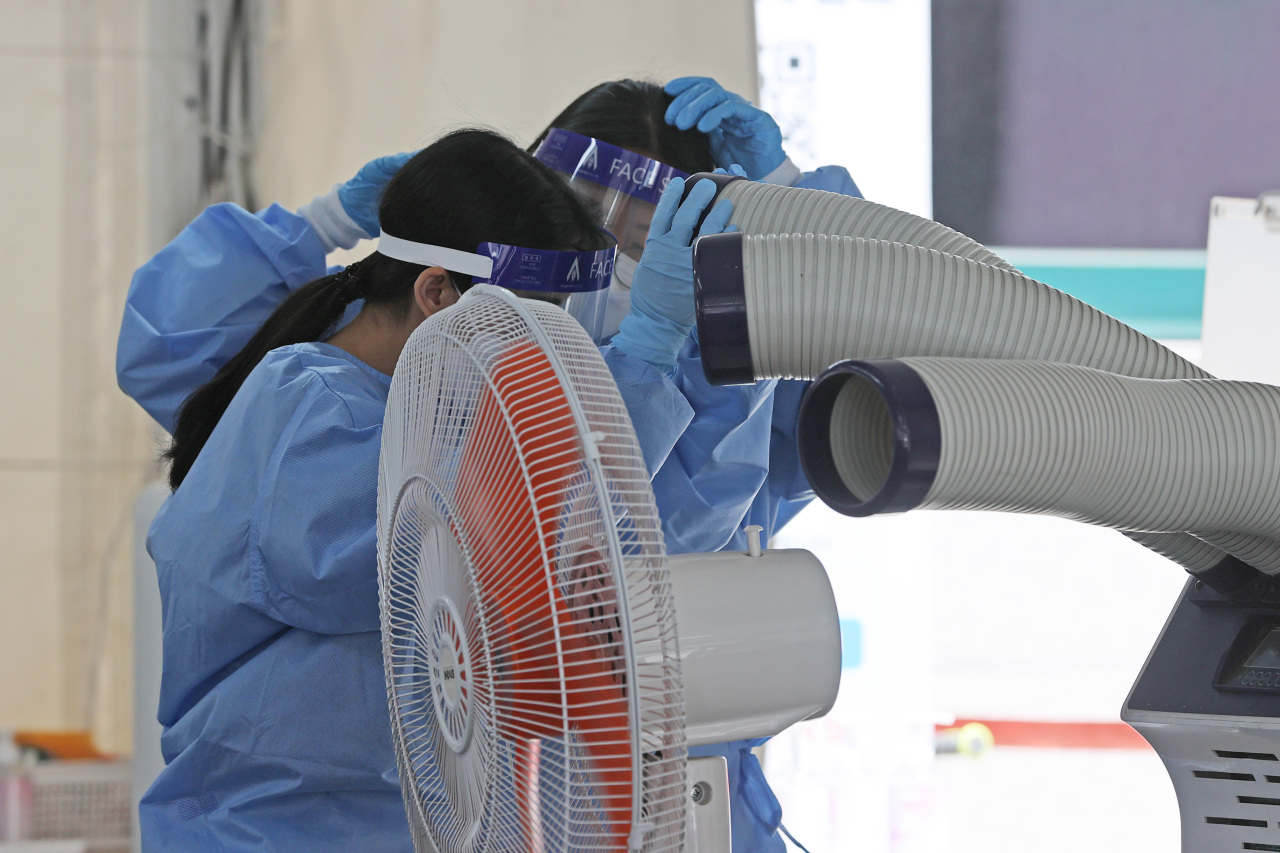 Medical workers stand in front of an evaporative air cooler at a COVID-19 test center in southern Seoul on Wednesday, amid early summer temperatures across the nation. (Yonhap)