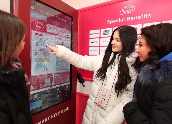 Foreigners look at the promotion signboard for a nationwide event -- under which the government and companies provide inbound visitors with a variety of discounts in segments such as shopping, transportation and lodging -- in downtown Seoul in January 2020. (Ministry of Culture, Sports and Tourism)