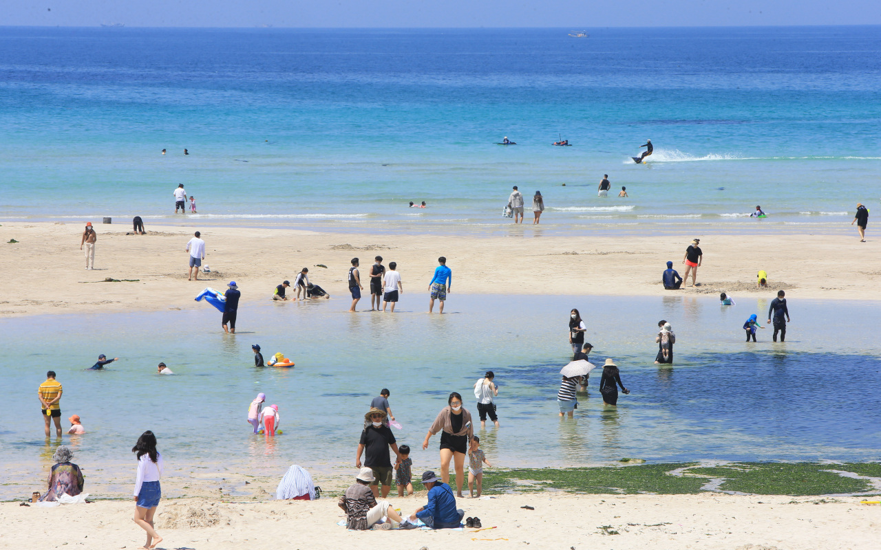 Tourists play in the water on Hamdeok Beach on Jeju Island on May 23, 2021. (Yonhap)