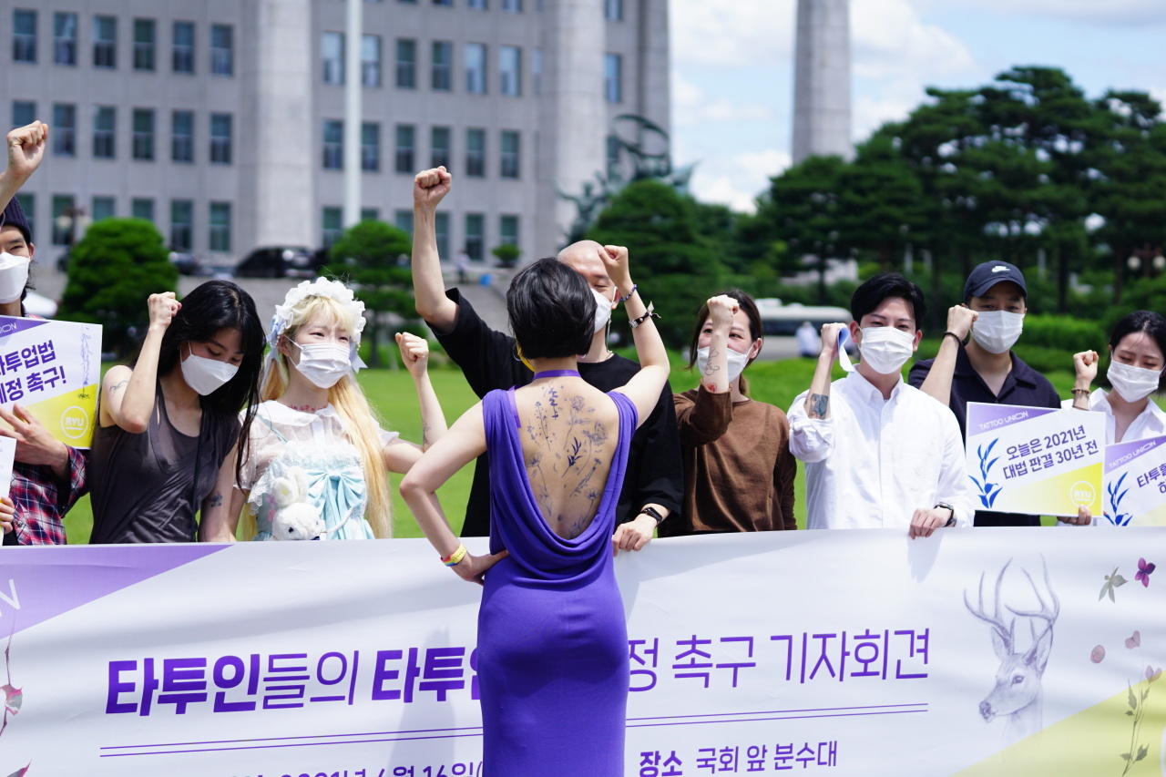 Rep. Ryu Ho-jeong (center) of the minor Justice Party shouts out slogans during a press conference held at the National Assembly to demand changes to “outdated” laws on tattoos. Ryu wore a purple backless dress to show off her temporary body art as a means to show her support for tattooing as an acceptable form of expression. (Office of Rep. Ryu Ho-jeong/Yonhap)
