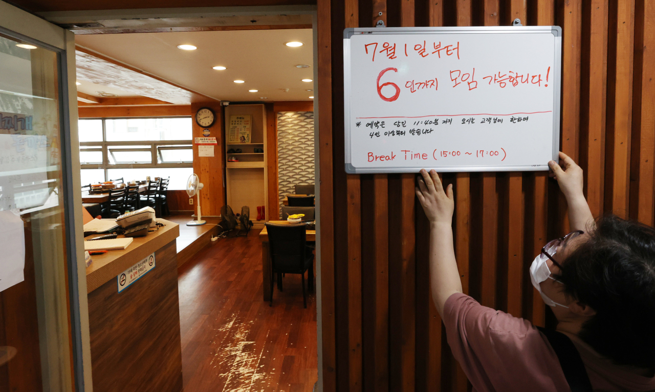 An employee puts up a sign at a restaurant in Seoul on Monday, to inform customers that gatherings of up to six people are allowed starting Thursday under the eased social distancing rules amid the coronavirus pandemic. Under the new Level 2 distancing, the ban on gatherings of five or more people will be eased to six people until July 14 in the greater Seoul area after which the ceiling will go up to eight. (Yonhap)