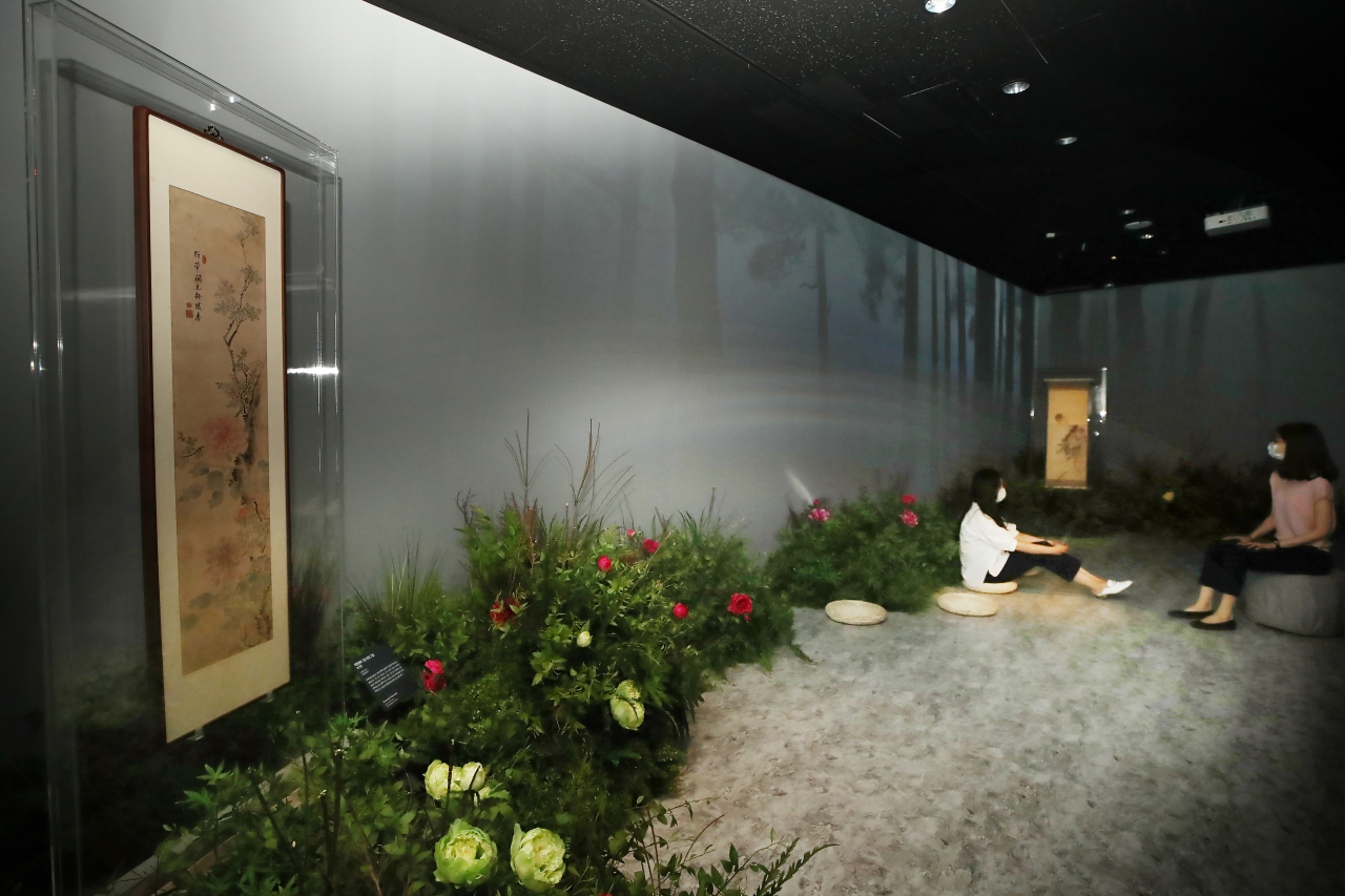 Visitors sit in a garden with peonies and peony paintings. (Yonhap)