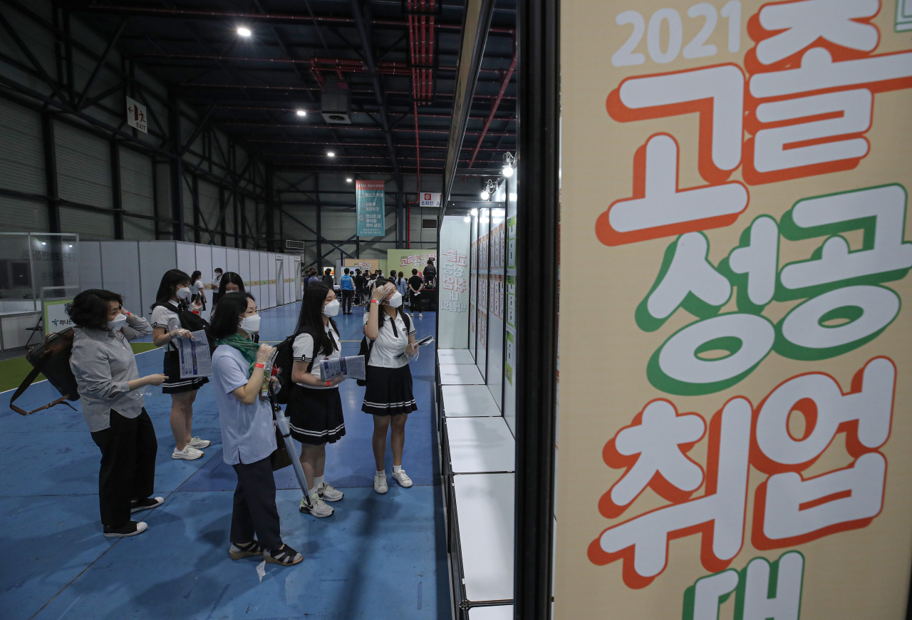 This June 15, 2021, file photo shows students looking at recruitment flyers on a bulletin board put up at a job fair held in Seoul. (Yonhap)