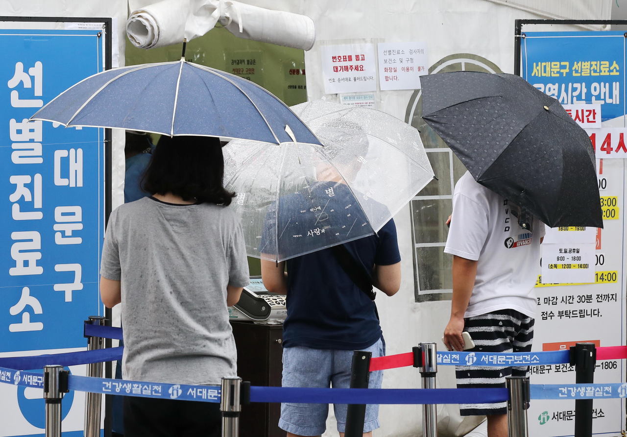 People wait in line to get tested for COVID-19 at a screening center in western Seoul on Sunday. (Yonhap)