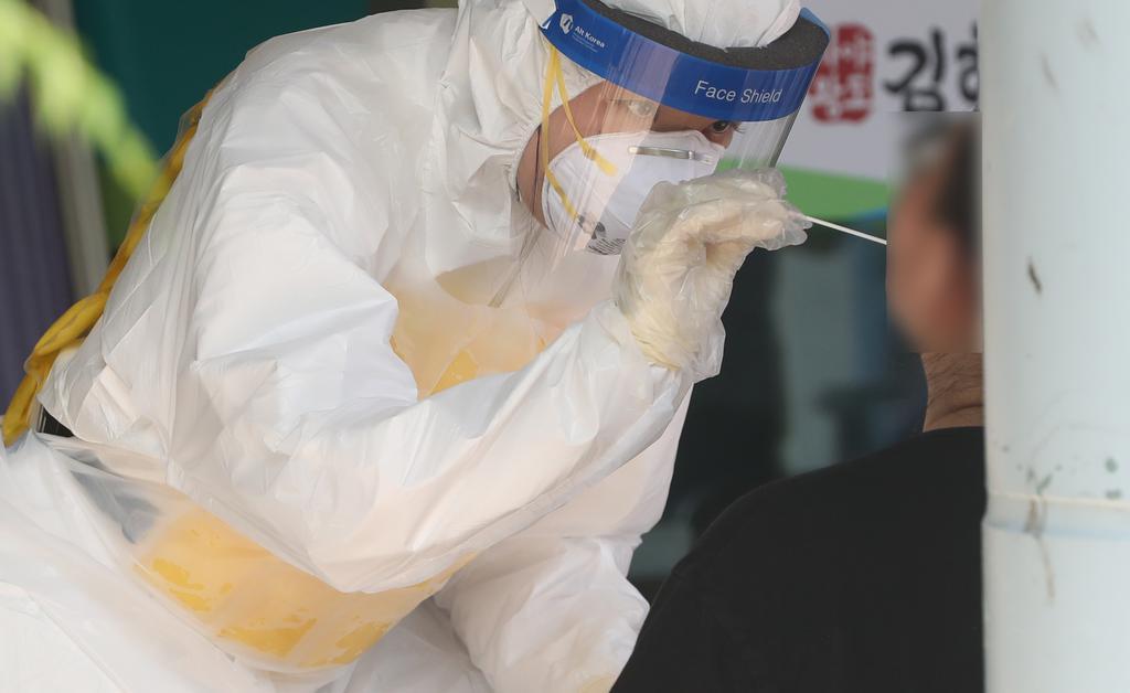 A health worker in a protective suit collects a sample from a citizen at a virus testing clinic in Gimhae, South Gyeongsang Province, on Wednesday. (Yonhap)