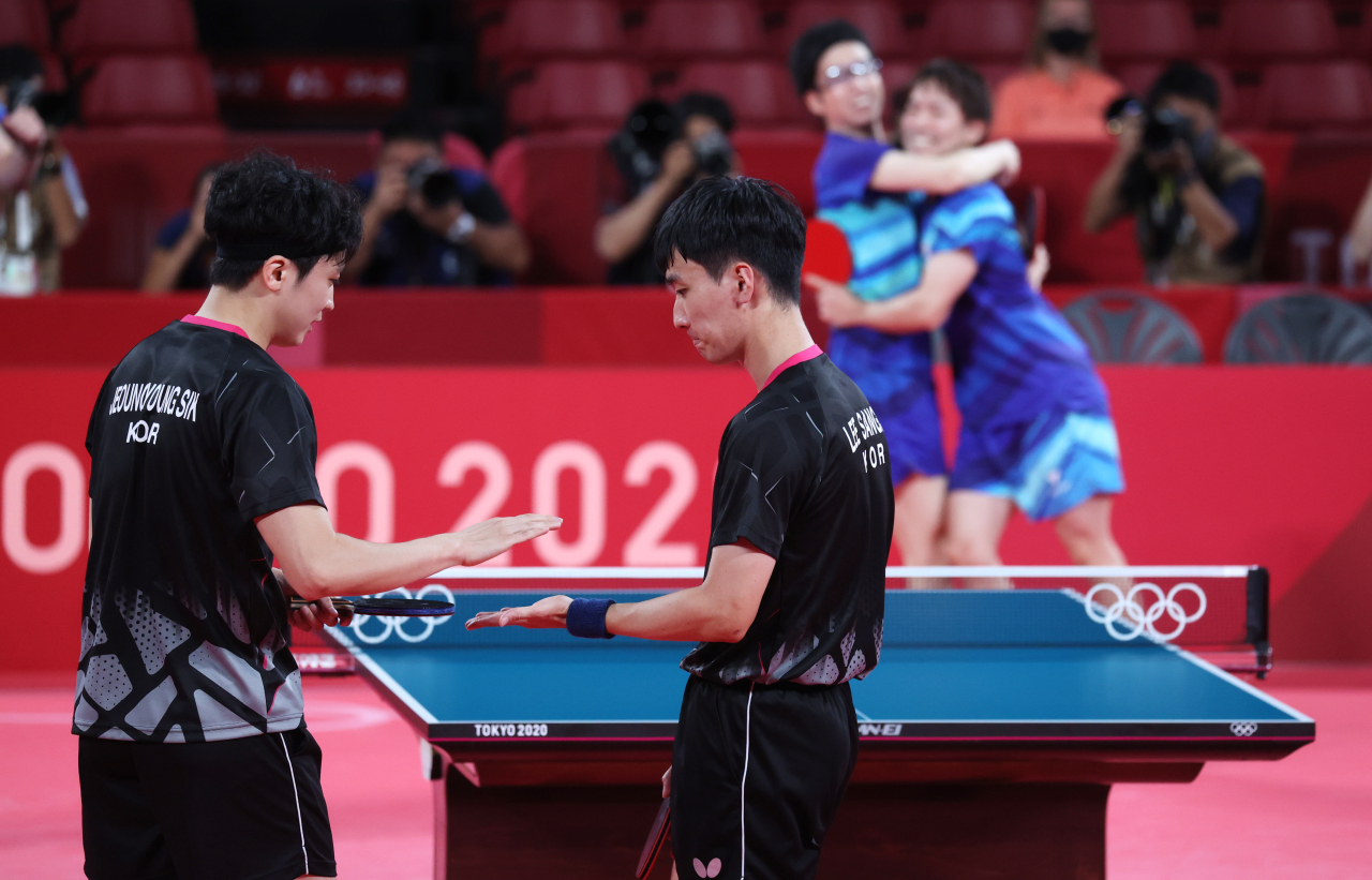 Jeoung Young-sik(L) and Lee Sang-su of South Korea react to their doubles loss to Jun Mizutani and Koki Niwa of Japan in the bronze medal match for the men's table tennis team event at the Tokyo Olympics at Tokyo Metropolitan Gymnasium in Tokyo on Friday. (Yonhap)
