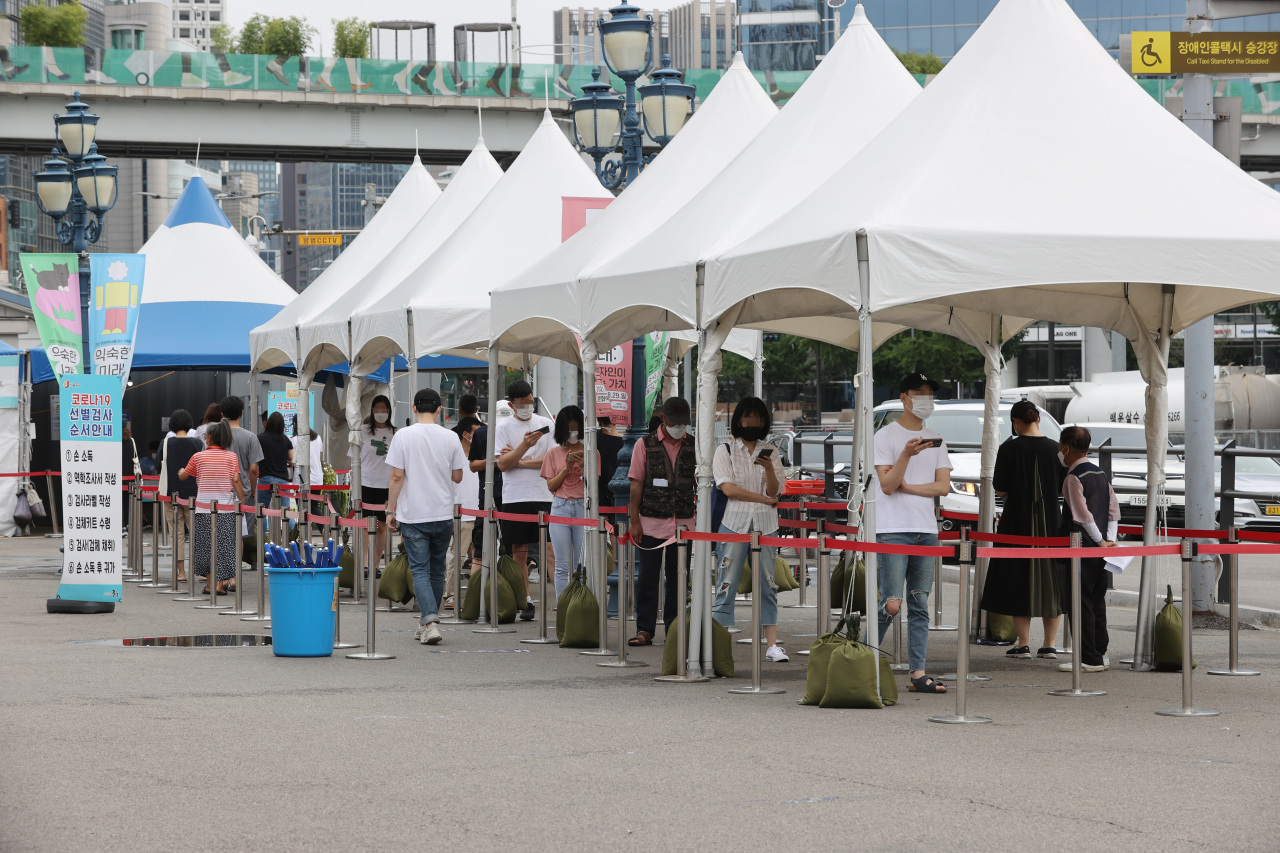 People wait in line to receive COVID-19 tests at a makeshift testing center in front of Seoul Station in central Seoul on Sunday. (Yonhap)