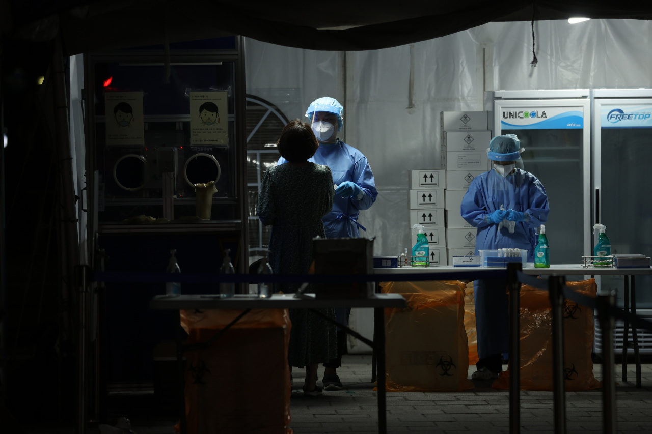 A worker at a COVID-19 testing center in southern Seoul collects test samples from a visitor on Thursday, as South Korea struggles to contain the fourth wave of the pandemic. (Yonhap)