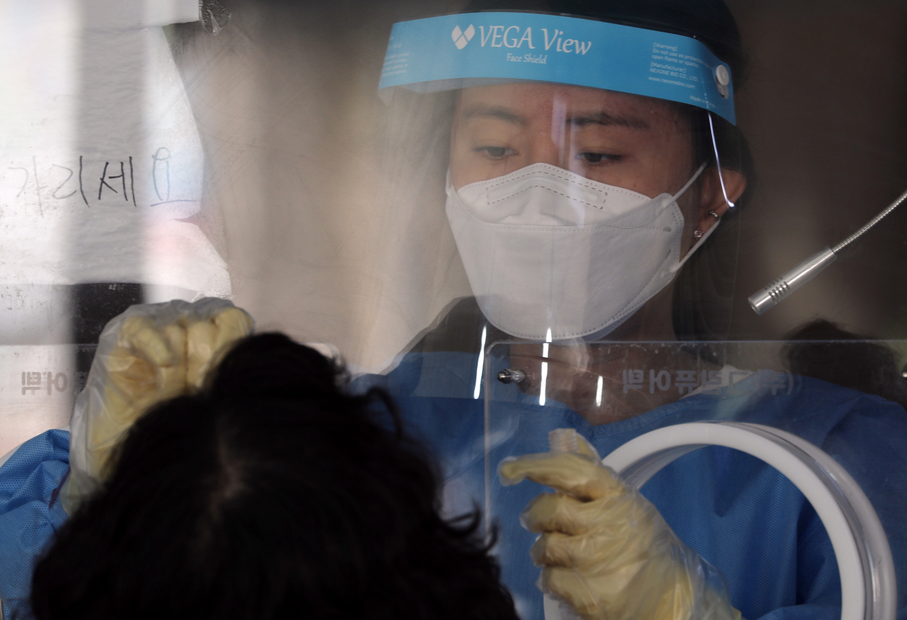 Health care worker takes a nasal swab sample from a woman at a Seoul testing center on Tuesday. (Yonhap)