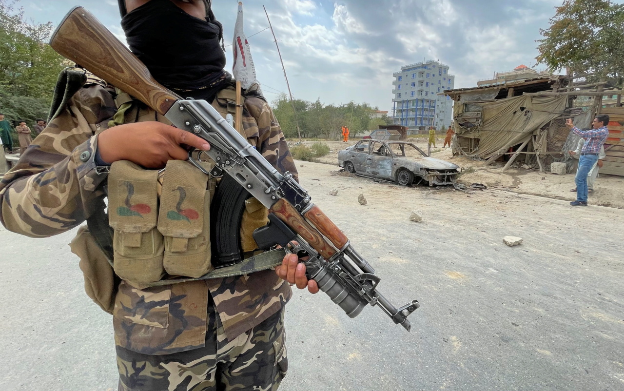 A member of Taliban forces stands guard as Afghan men take pictures of a vehicle from which rockets were fired, in Kabul, Afghanistan Aug. 30. (Reuters-Yonhap)