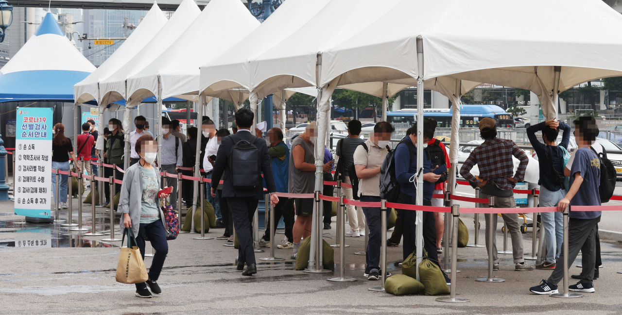 People stand in line to get COVID-19 tests in a screening station in front of Seoul Station on Friday. (Yonhap)