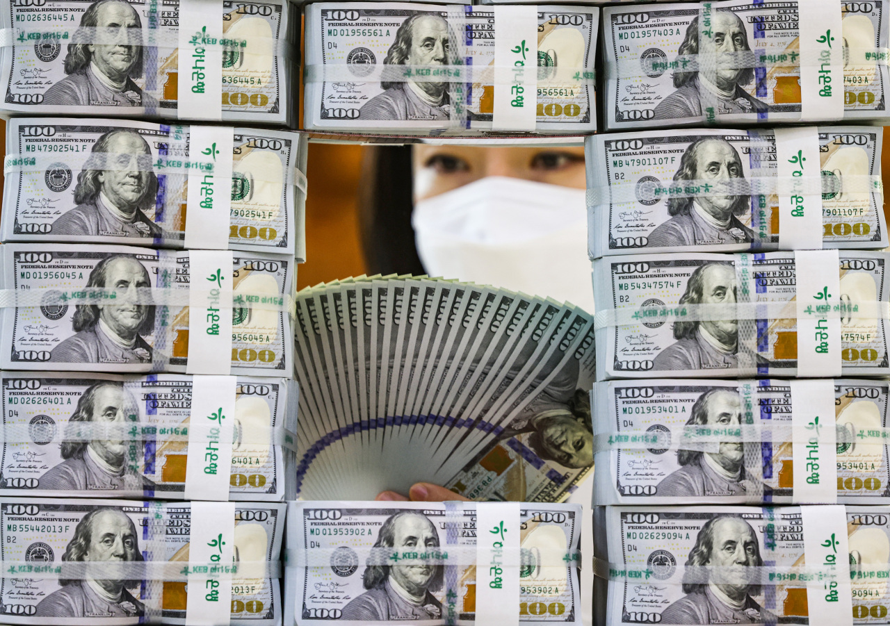 An employee counts money next to stacks of US dollar banknotes at KEB Hana Bank’s headquarters in Seoul, Wednesday. (Yonhap)