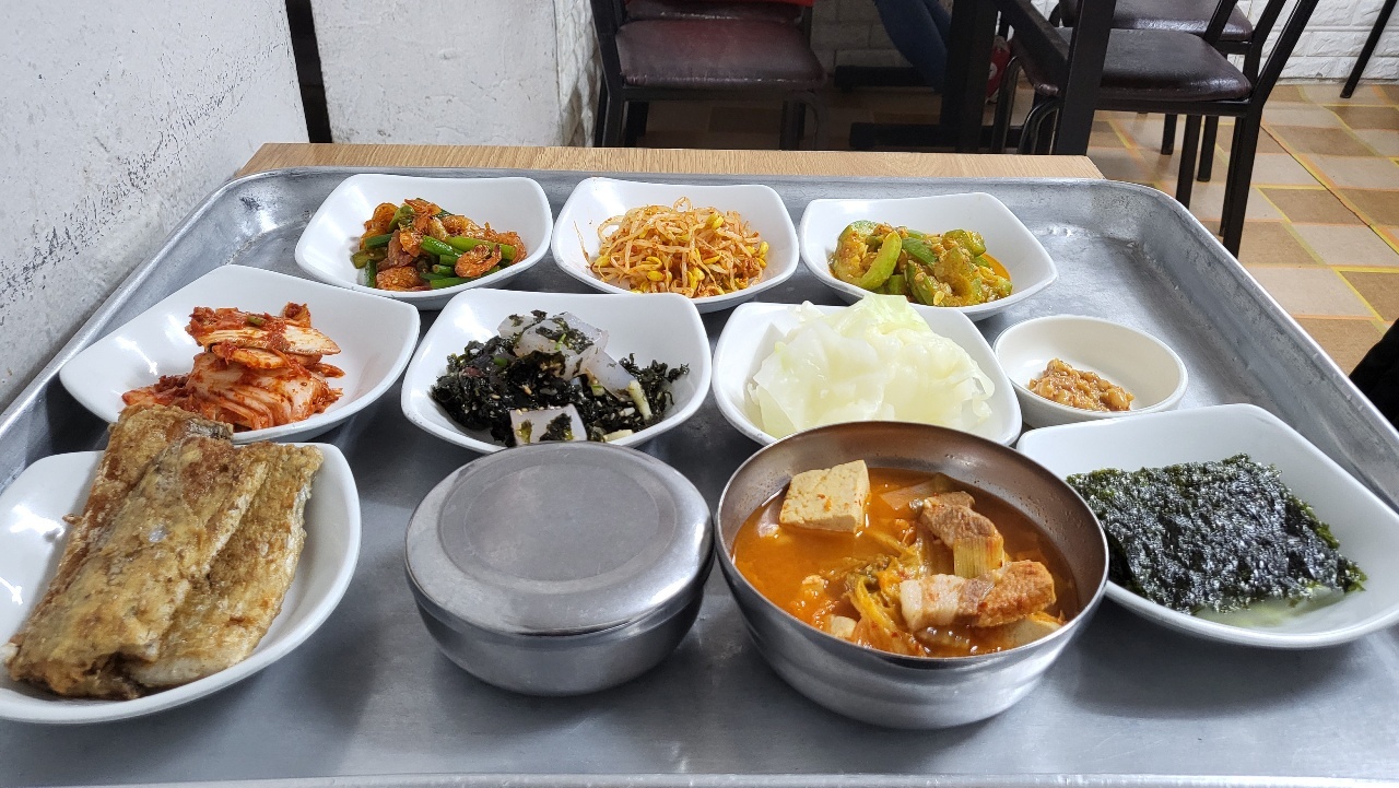 The Yangji sikdang (From top-left to bottom-right) geonsaeu maneuljong bokkeum (stir-fried shrimp with garlic scapes), kongnamul muchim (seasoned soybean sprouts), aehobak bokk-eum (stir-fried Korean zucchini), baechukimchi(cabbage kimchi), chungpomuk gimmuchim (seasoned mung bean jelly with seaweed), yangbaechu dechim and doenjang(boiled cabbage with Korean miso sauce), galchigui (pan-fried cutlassfish), dubu dwaejigogi gimchijjigae (kimchi stew with tofu and pork), gim gu-i (roasted seaweed) (Kim Hae-yeon/ The Korea Herald)
