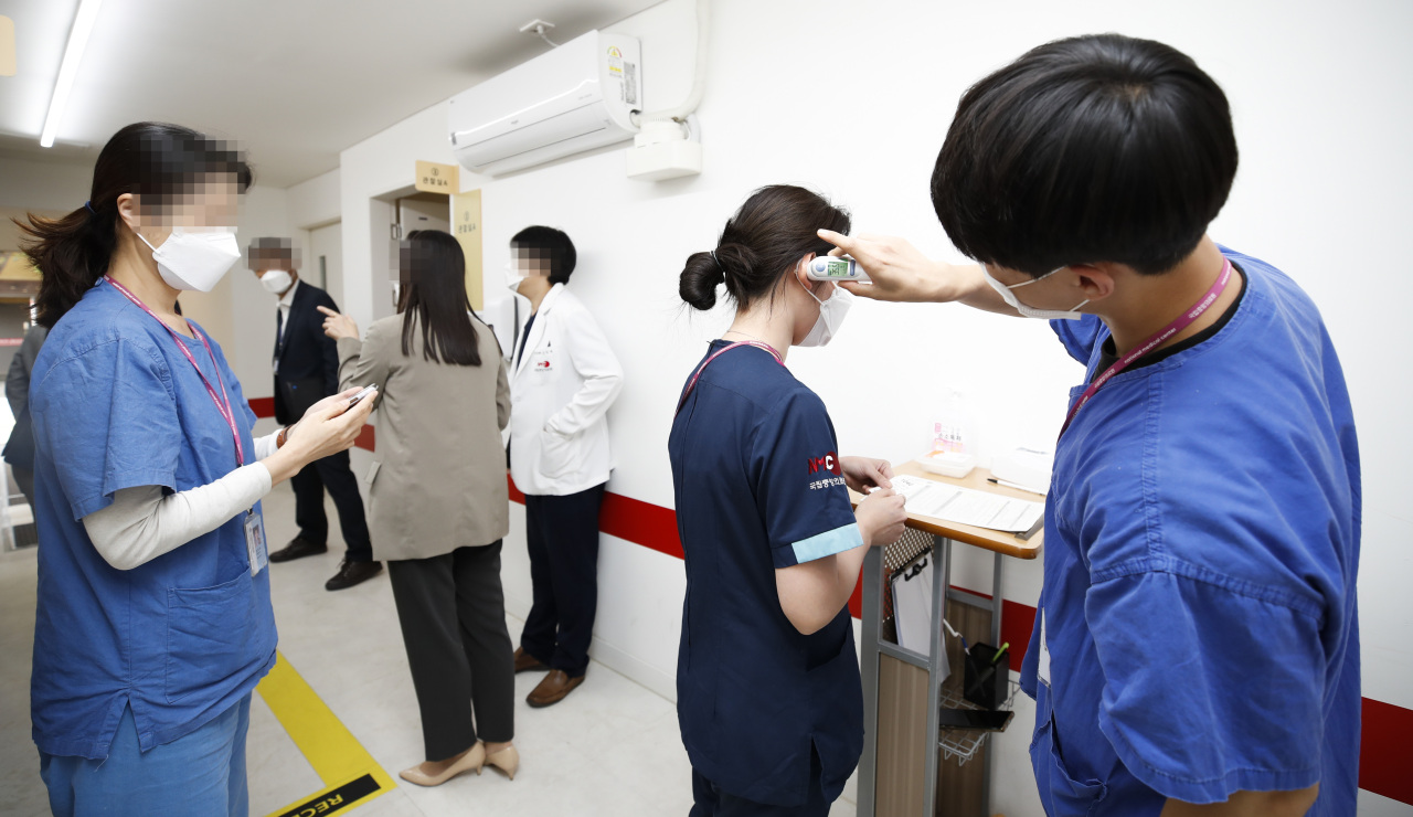 A medical worker (R) checks the body temperature of people who are set to receive additional vaccine jabs at a vaccination center in Seoul on Tuesday. Health authorities started giving additional COVID-19 shots to people who were fully vaccinated six months ago the same day. (Yonhap)