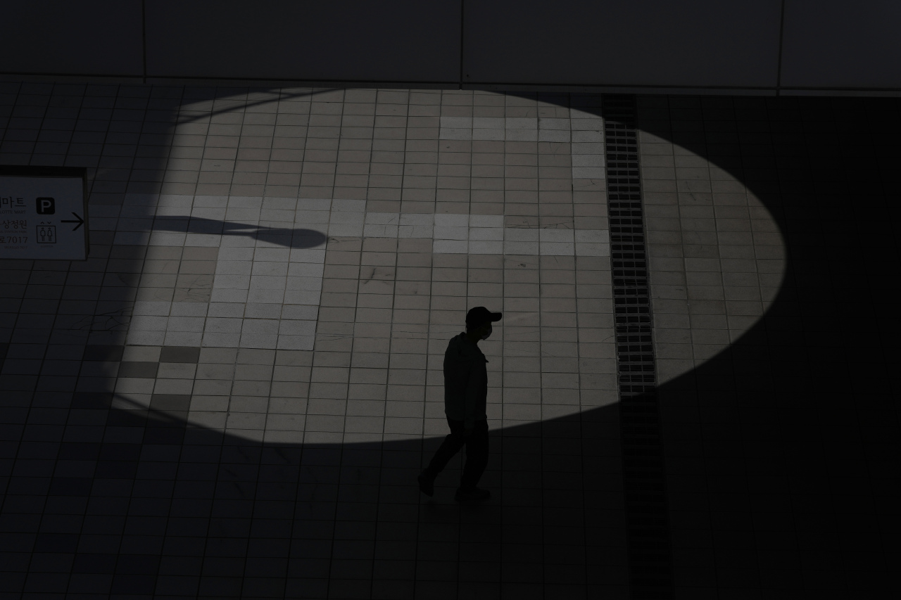 A visitor wearing a face mask to help curb the spread of the coronavirus is silhouetted while walking past outside of a shopping mall in September in Seoul, South Korea. (AP-Yonhap)