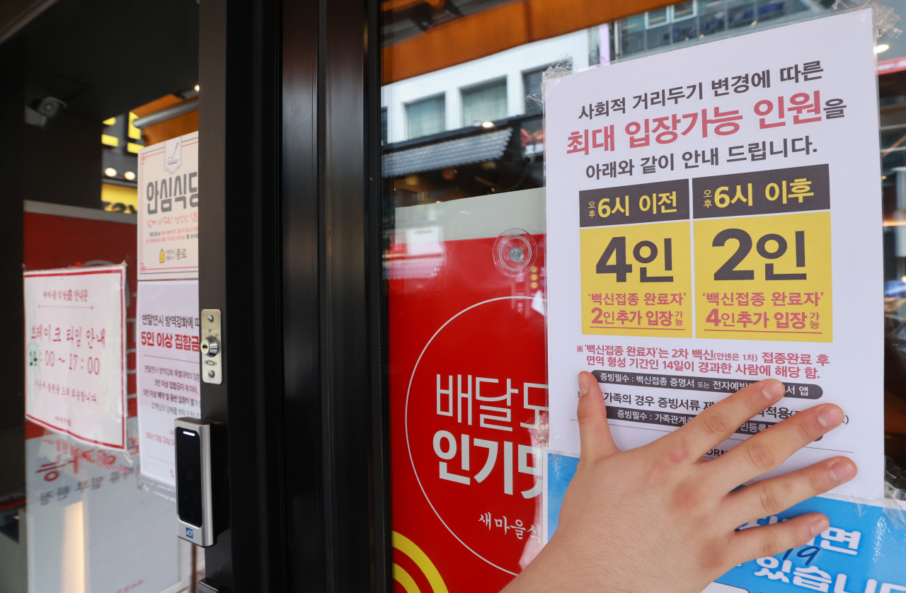 This photo taken on Sunday, shows a worker attaching a notice on the revised social distancing rules on the window of a restaurant in Seoul. (Yonhap)