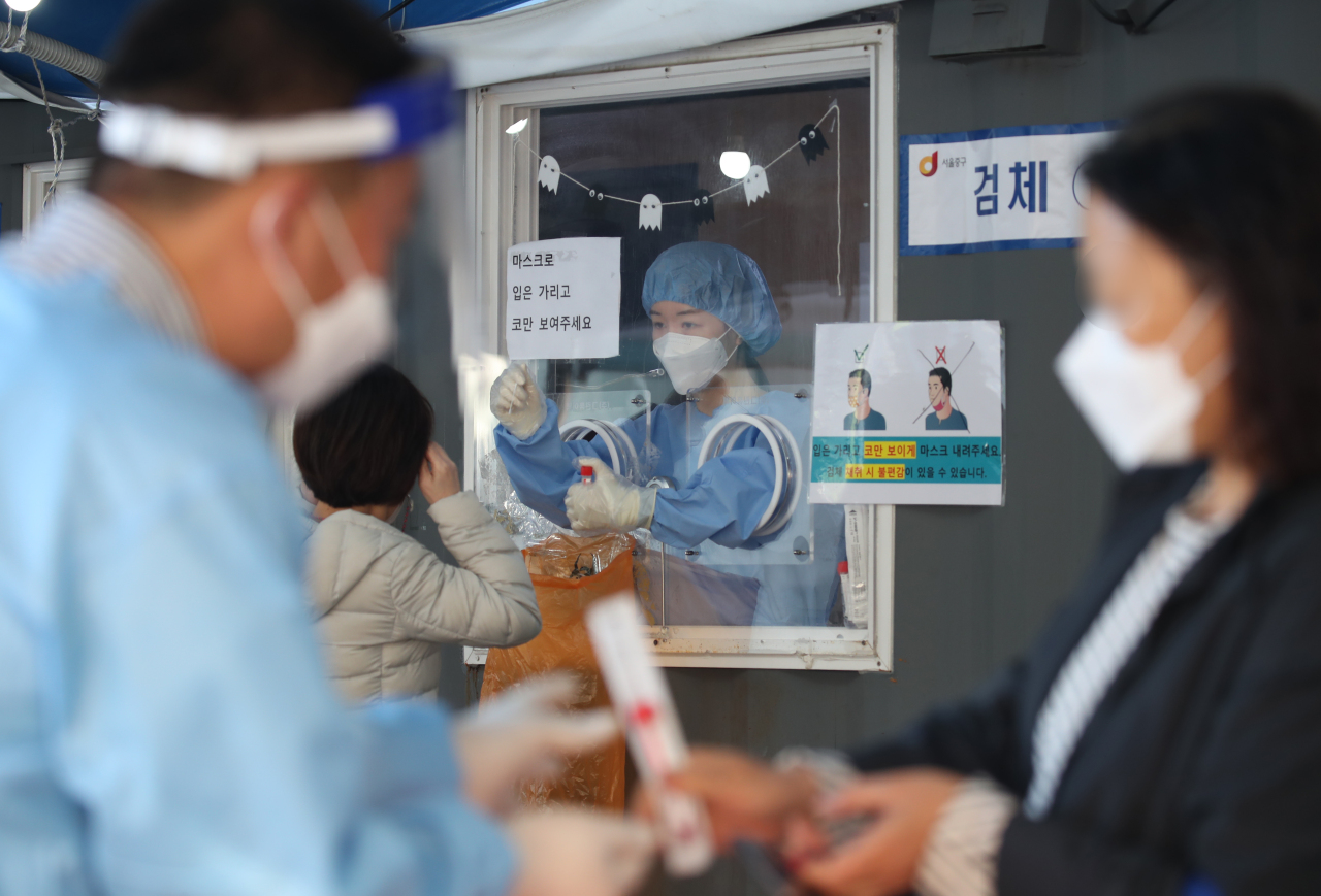 A health care worker is pictured taking a nasal swab from a woman at a testing center in central Seoul on Sunday. (Yonhap)